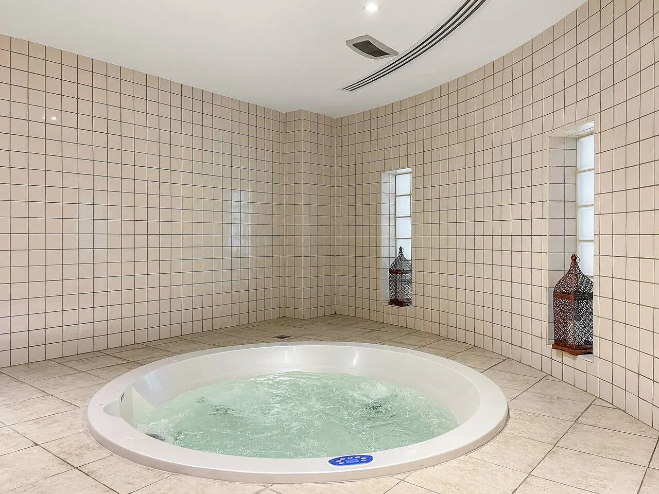 Una sala alicatada con una bañera de hidromasaje redonda y ventanas estrechas.