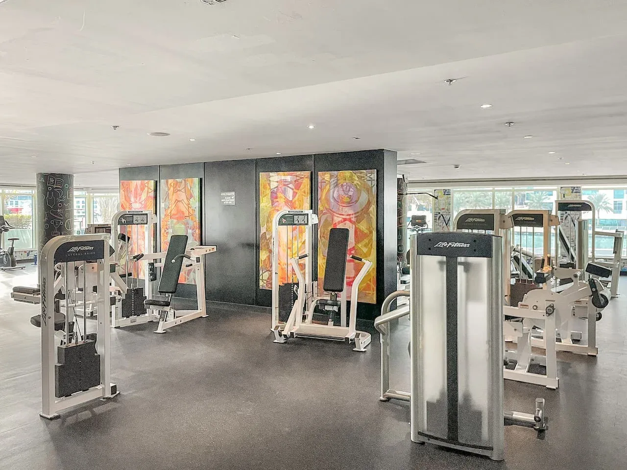 Un gimnasio con máquinas de ejercicio y obras de arte coloridas en las paredes.