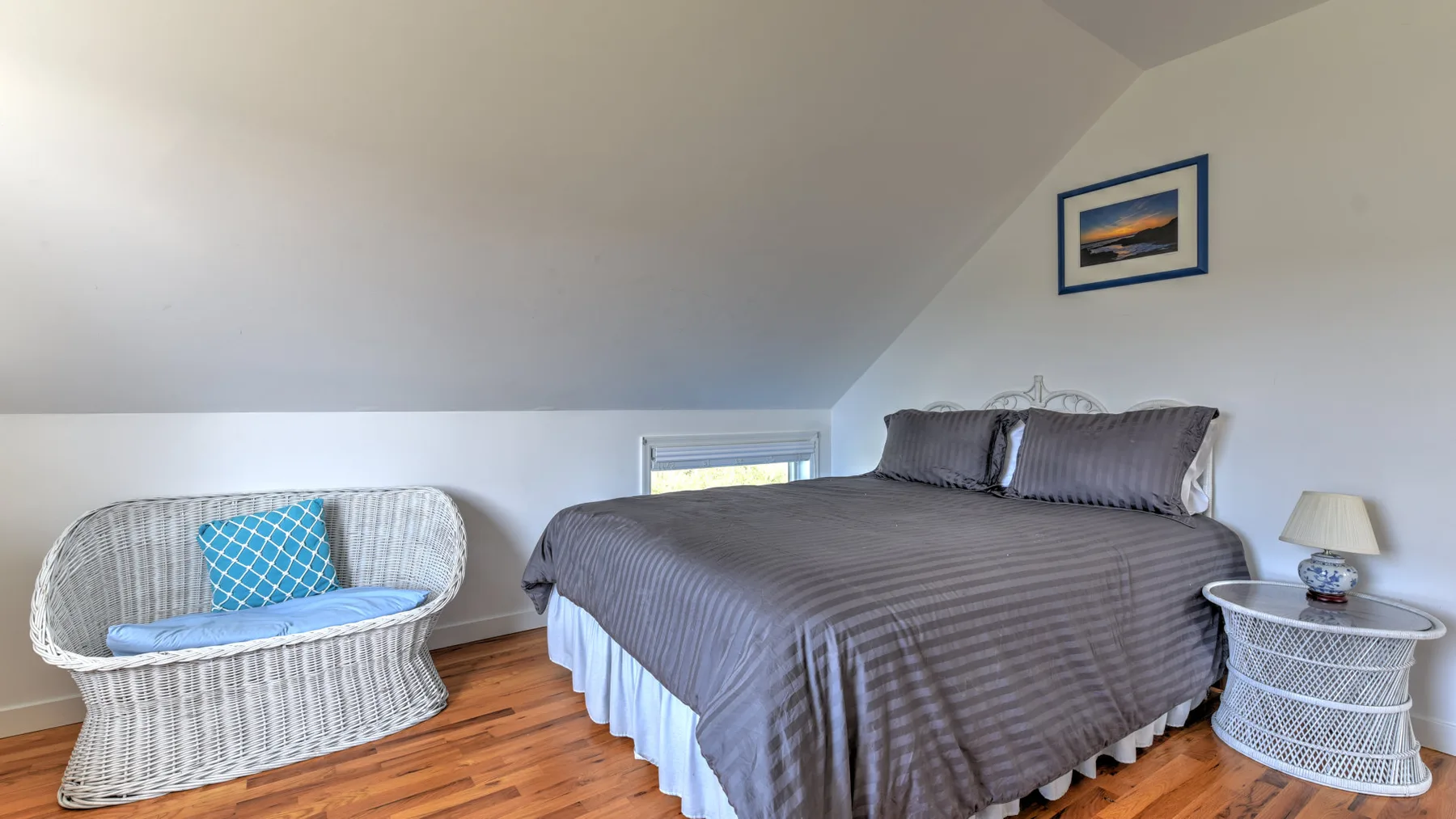 A bedroom with a large bed and a wicker loveseat beneath a sloped ceiling.