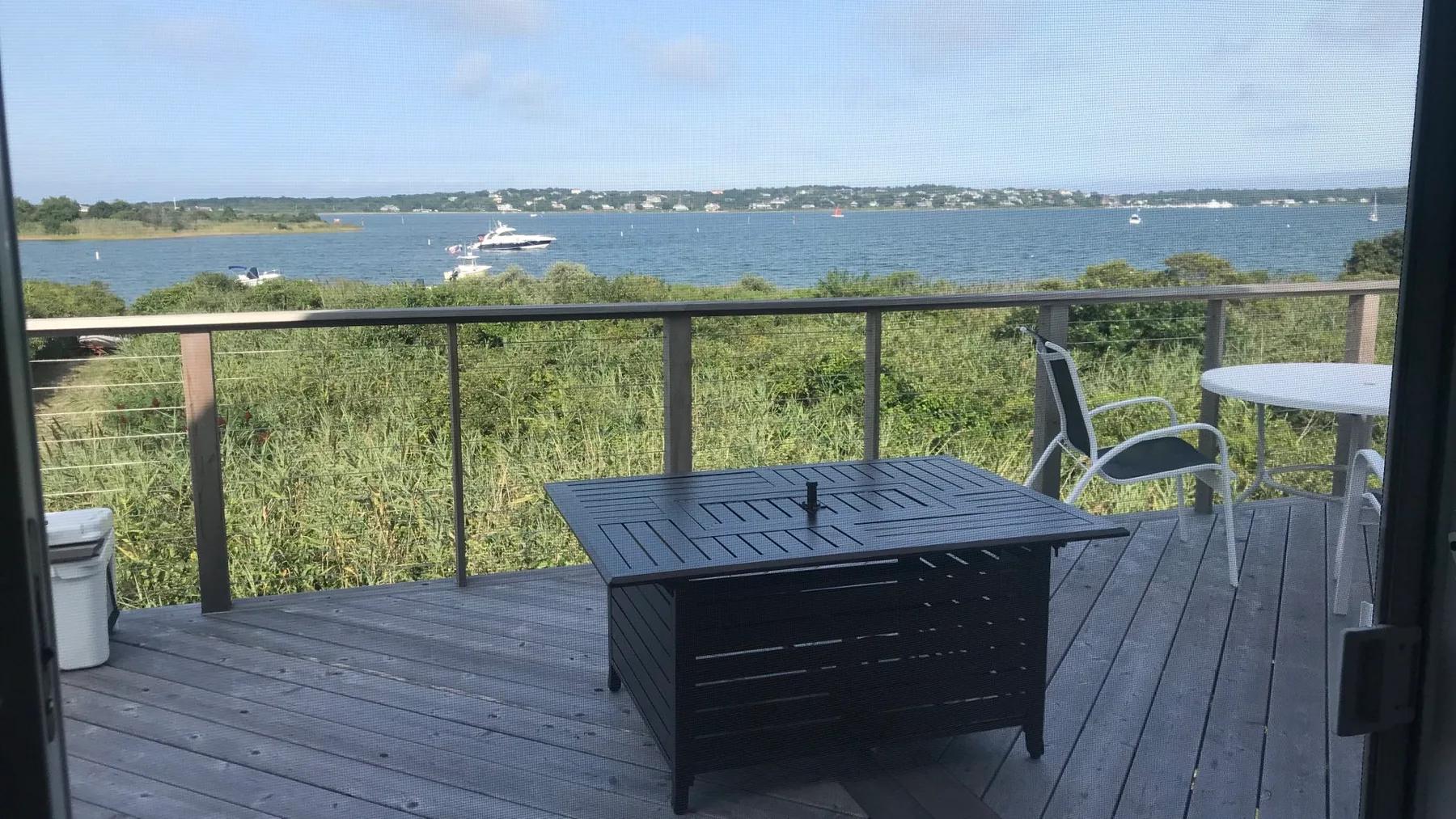 A waterfront deck with a black table and seating overlooks the water.