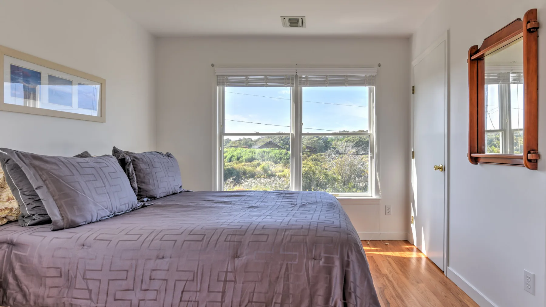 A bedroom with a bed beside a large window overlooking greenery.