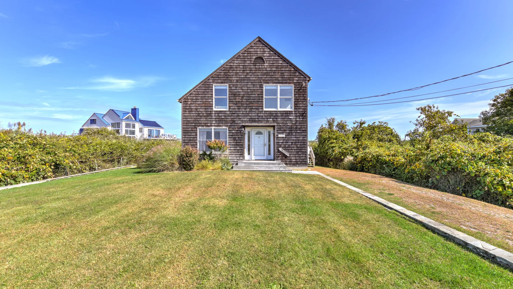 A dark-sided house stands beyond a broad lawn and beside a driveway.