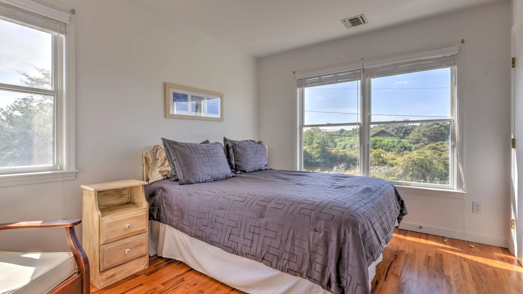 A bedroom with a bed covered in a gray quilt beside large windows.