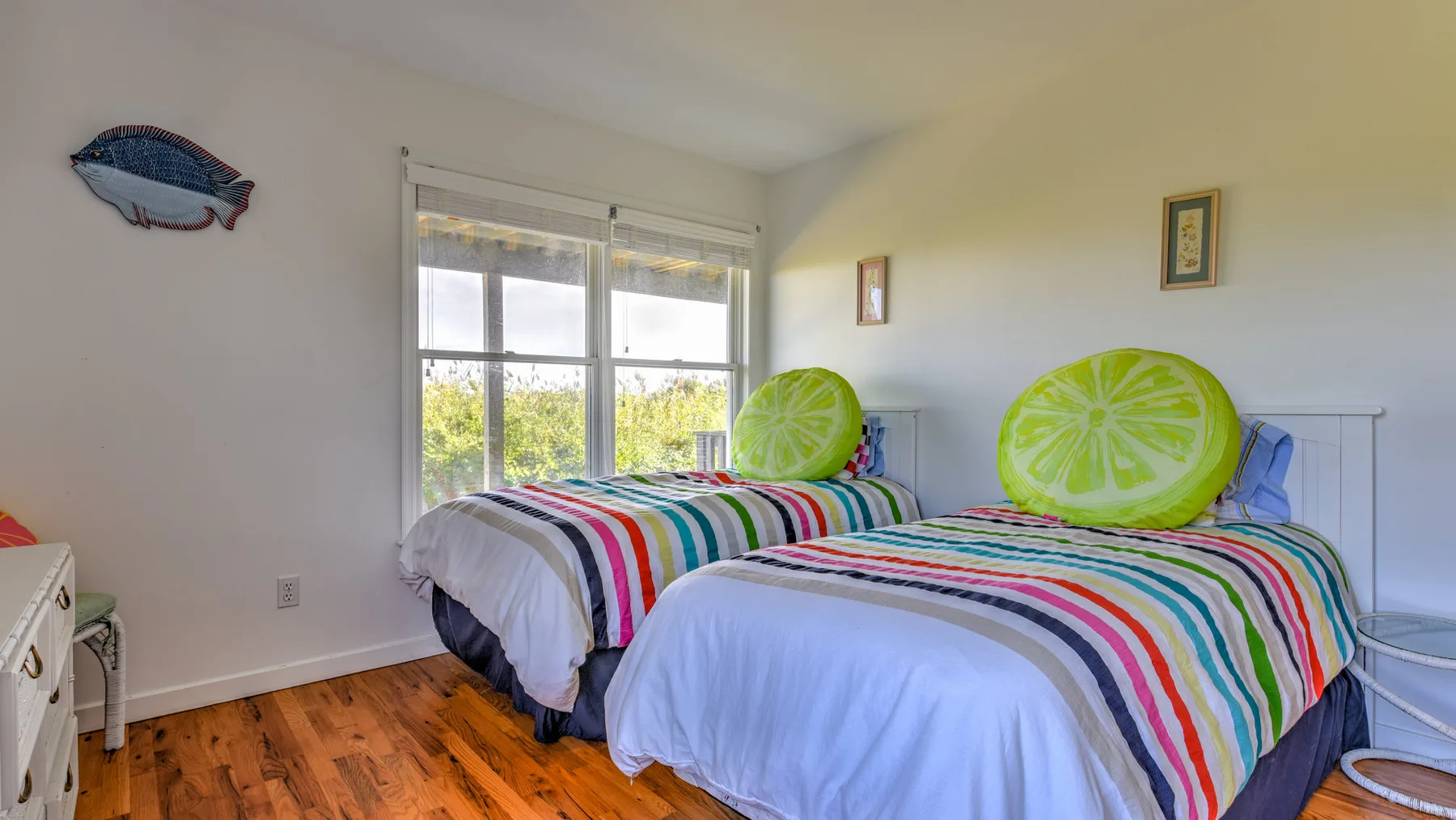 A bright bedroom with two beds covered in colorful striped bedding.