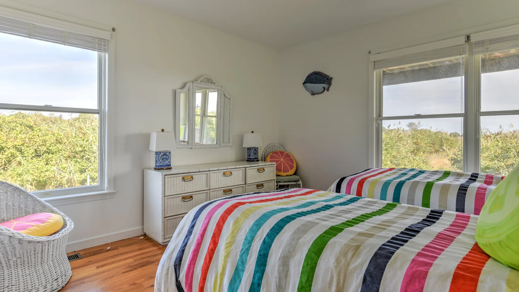 A bright bedroom with colorful striped bedding and windows overlooking greenery.