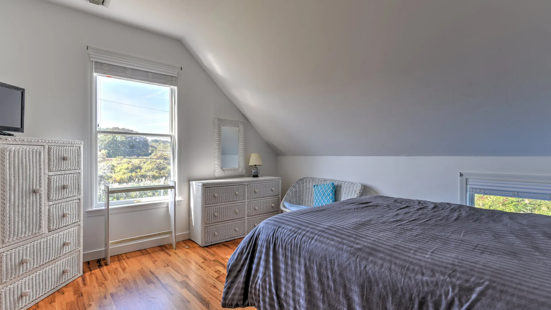 A bedroom with a bed, dressers, and windows beneath a sloped ceiling.
