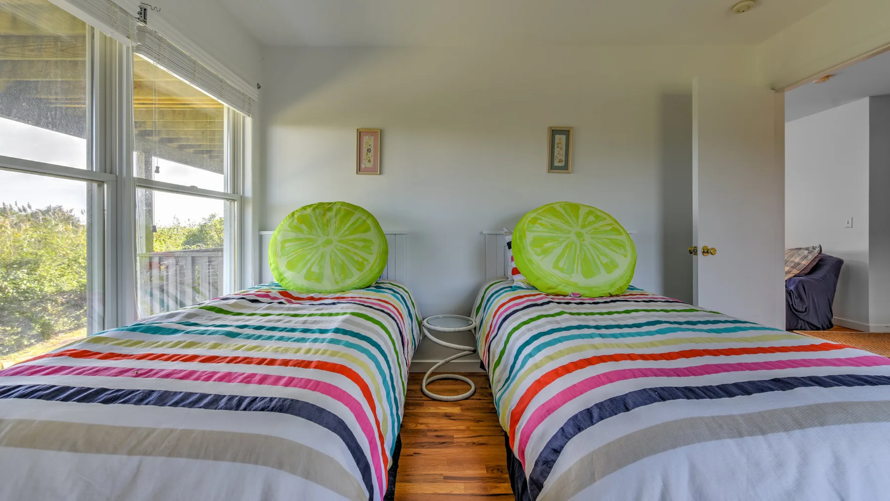 A bright bedroom with two beds covered in colorful striped bedding beside large windows.