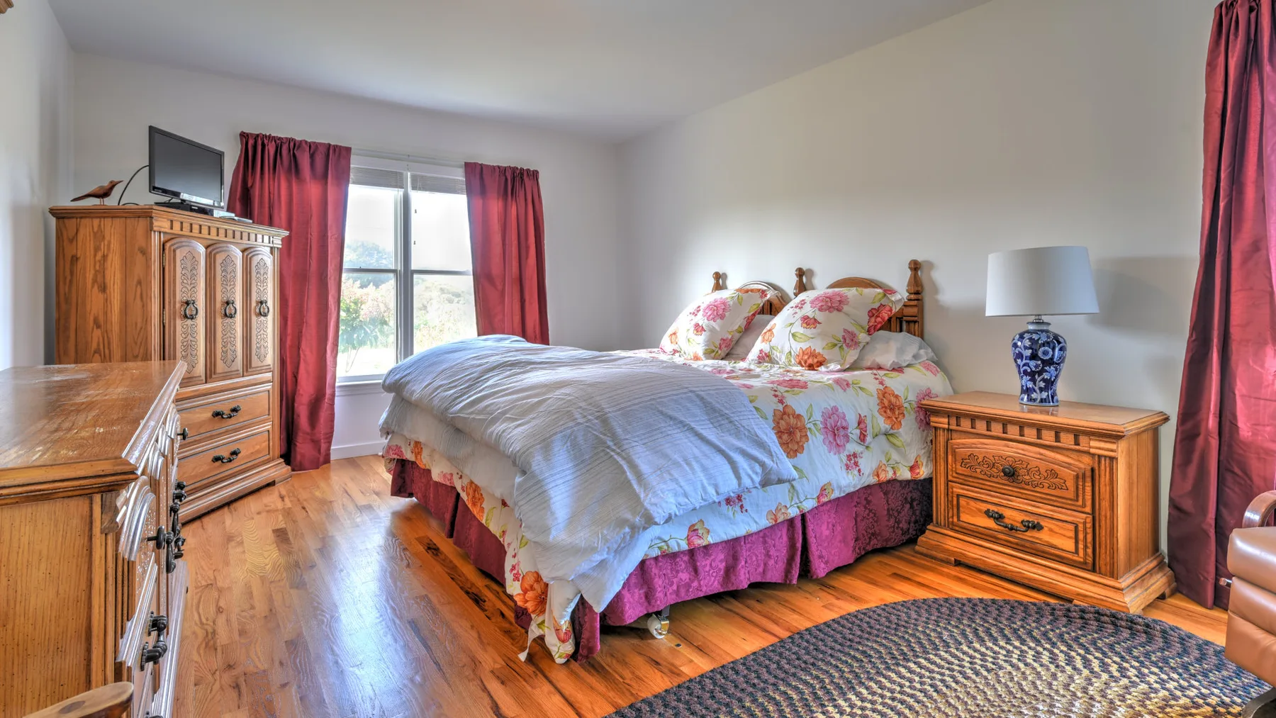 A bedroom with a bed covered in floral bedding and red curtains.