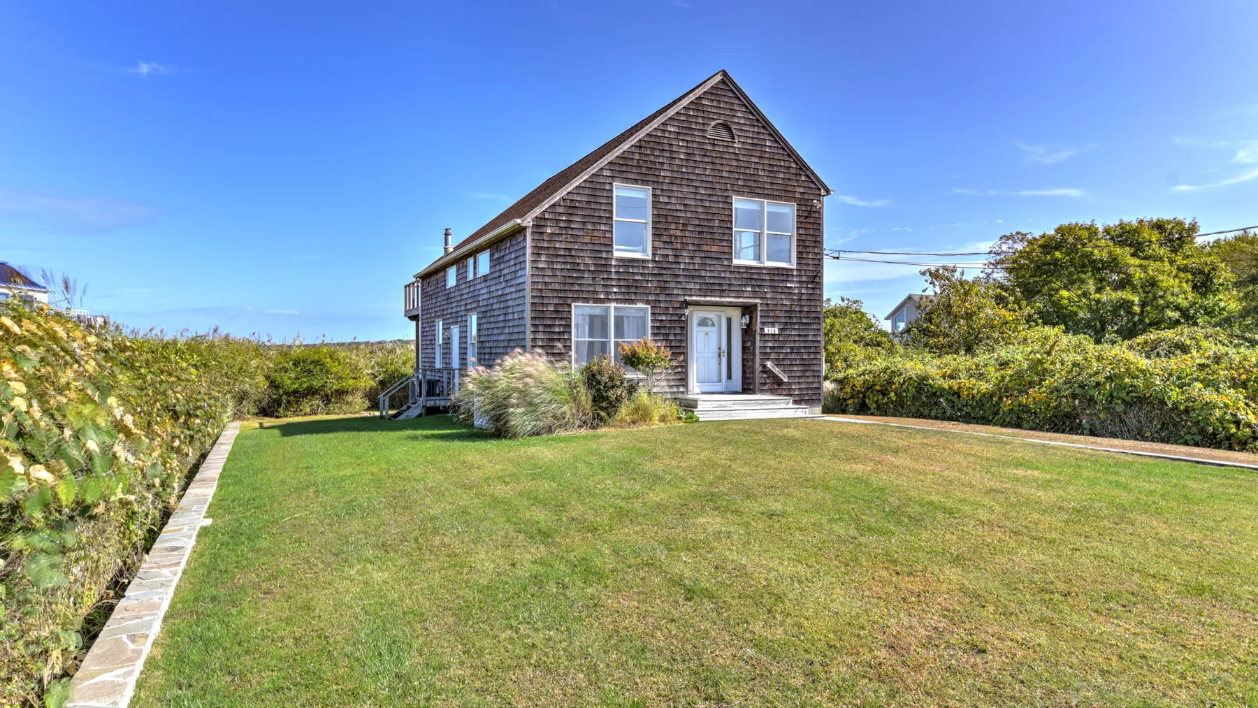 A dark-shingled house stands beyond a broad green lawn under a clear blue sky.