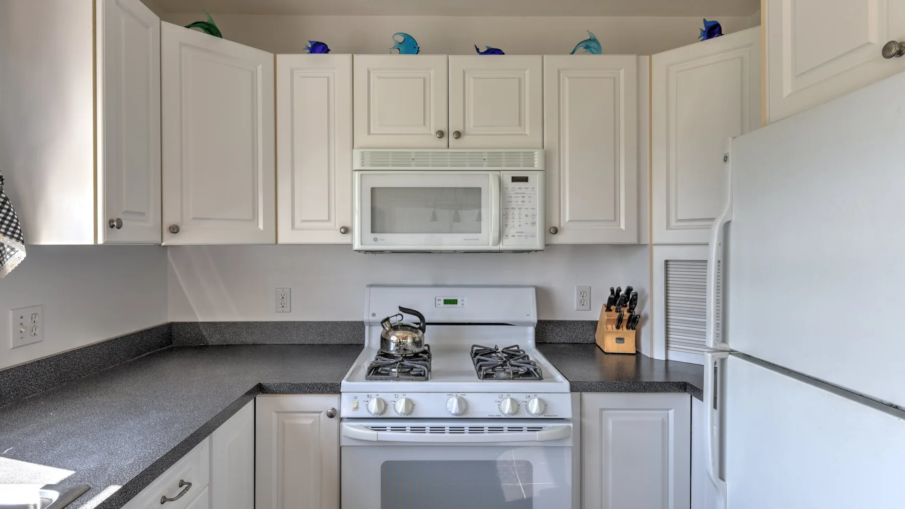 A bright kitchen with white cabinets, a stove, and dark countertops.