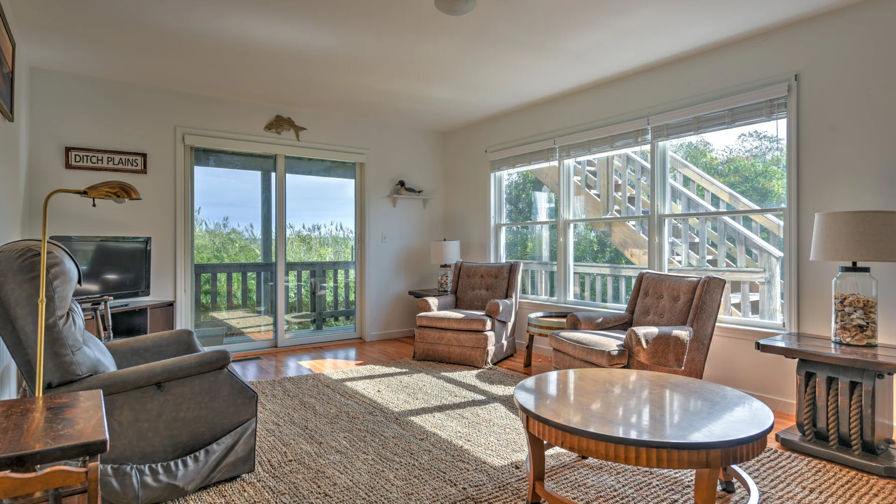 A bright living room with seating, a television, and large windows overlooking a deck.
