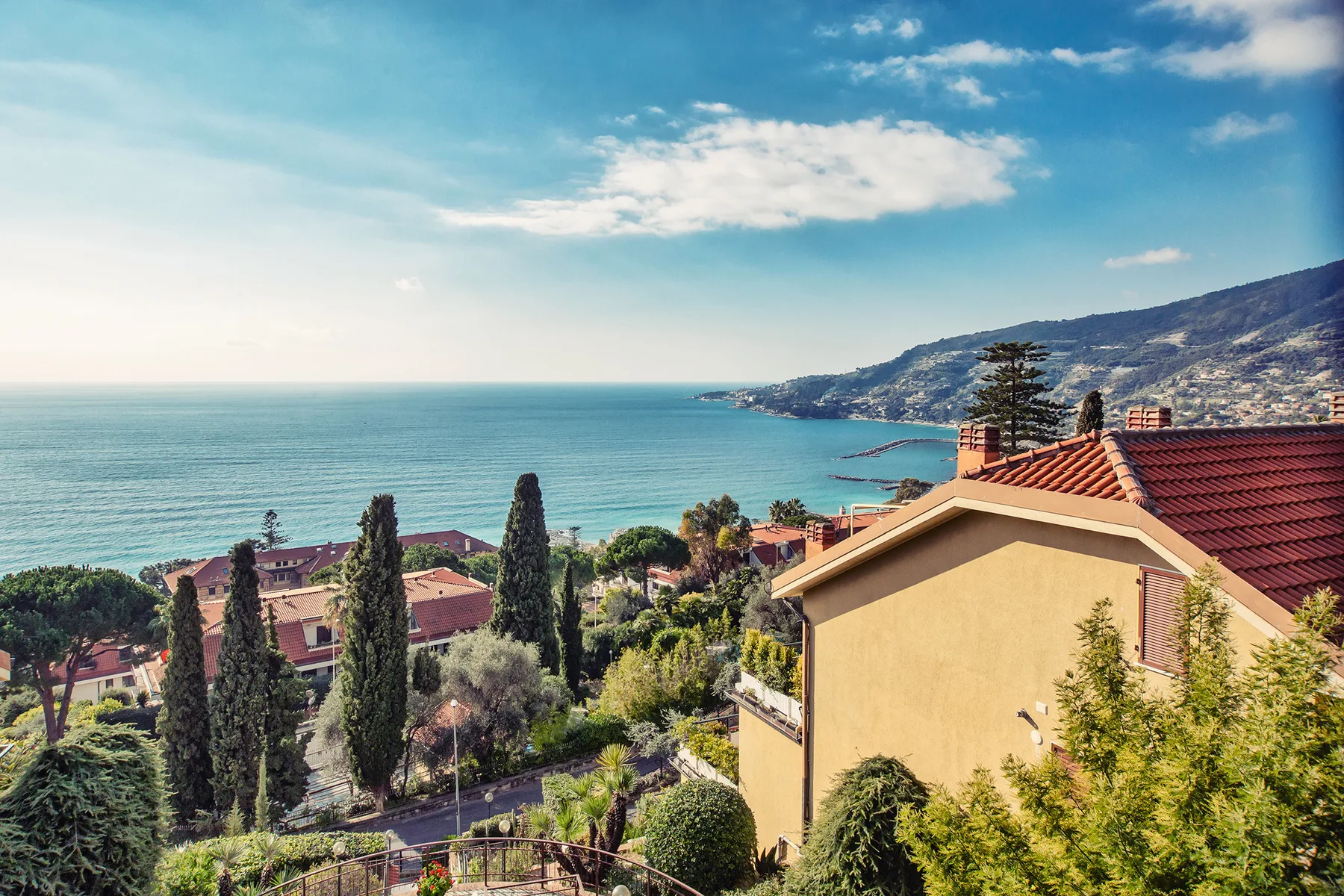 A coastal hillside neighborhood overlooks the sea, with homes and greenery in the foreground.