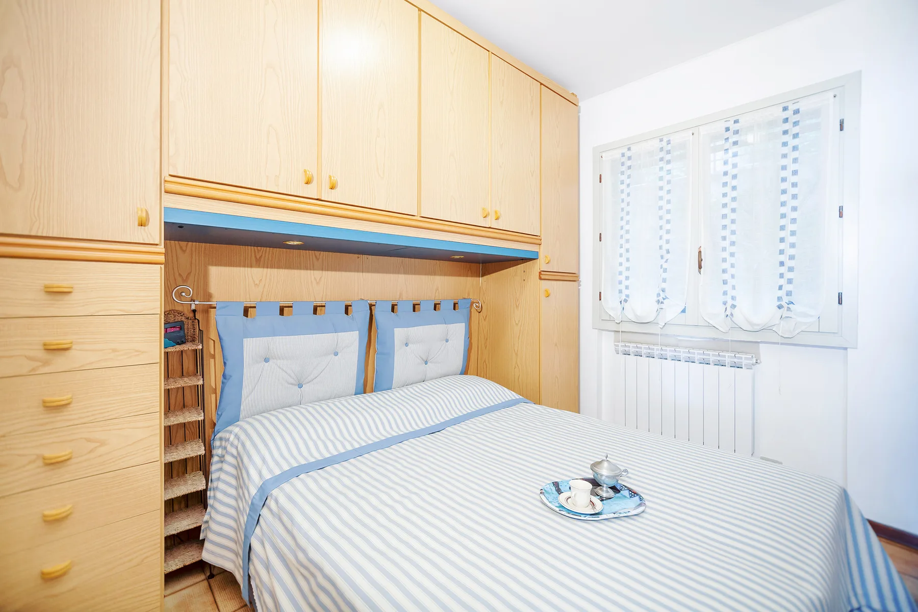 A bedroom with a neatly made bed beneath light wood cabinets.