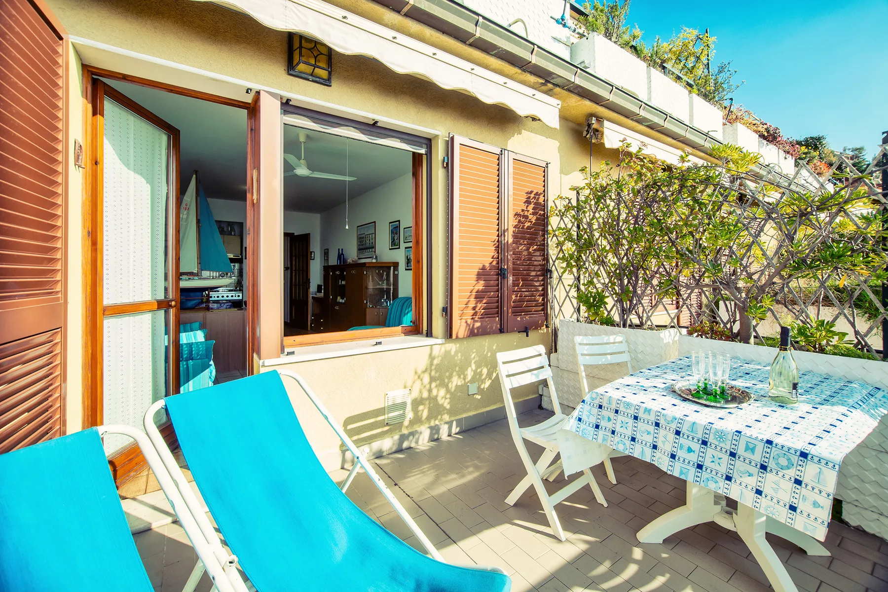 A sunny patio with turquoise lounge seating and a dining table beside open windows.