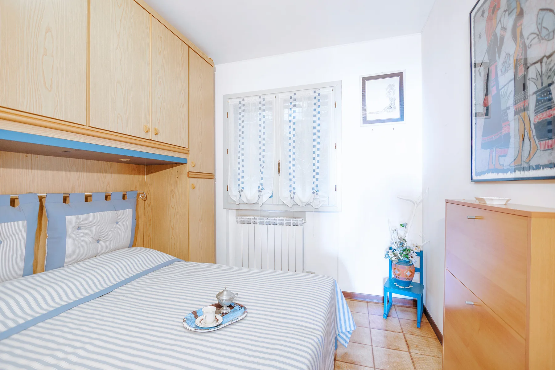 A bedroom with a striped bed beneath built-in wooden cabinets.