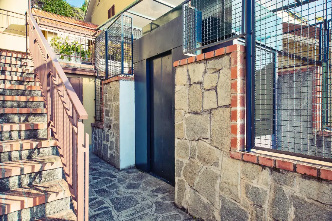 An outdoor stone-paved passage beside a staircase and a dark doorway.