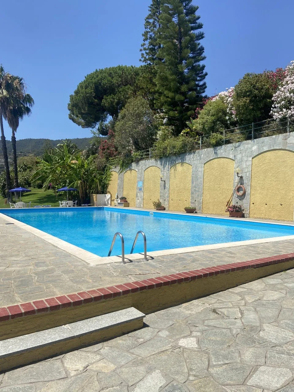 An outdoor swimming pool sits beside a stone patio and a garden wall.