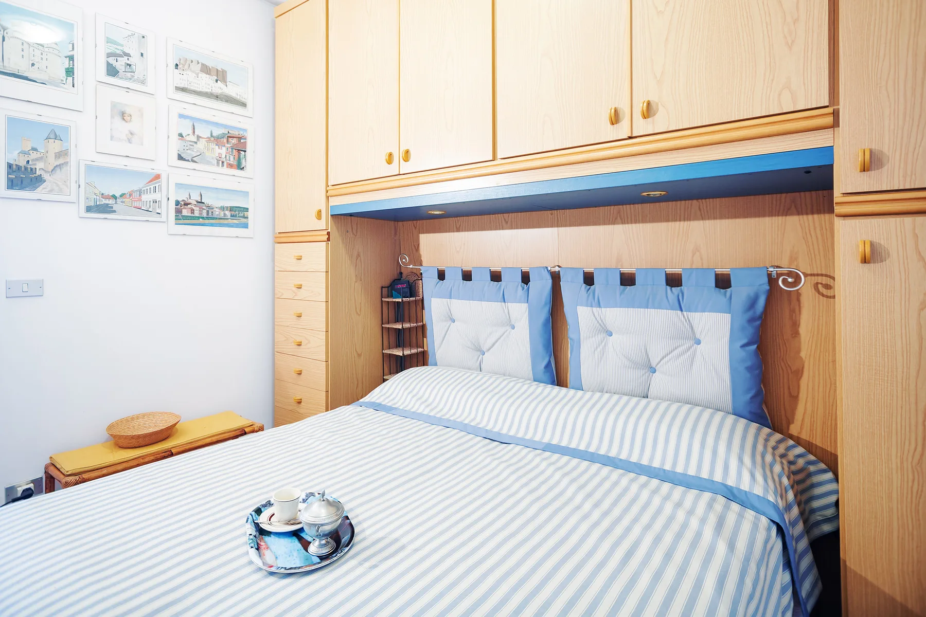 A bedroom with a blue-and-white striped bed beneath built-in wooden cabinets.