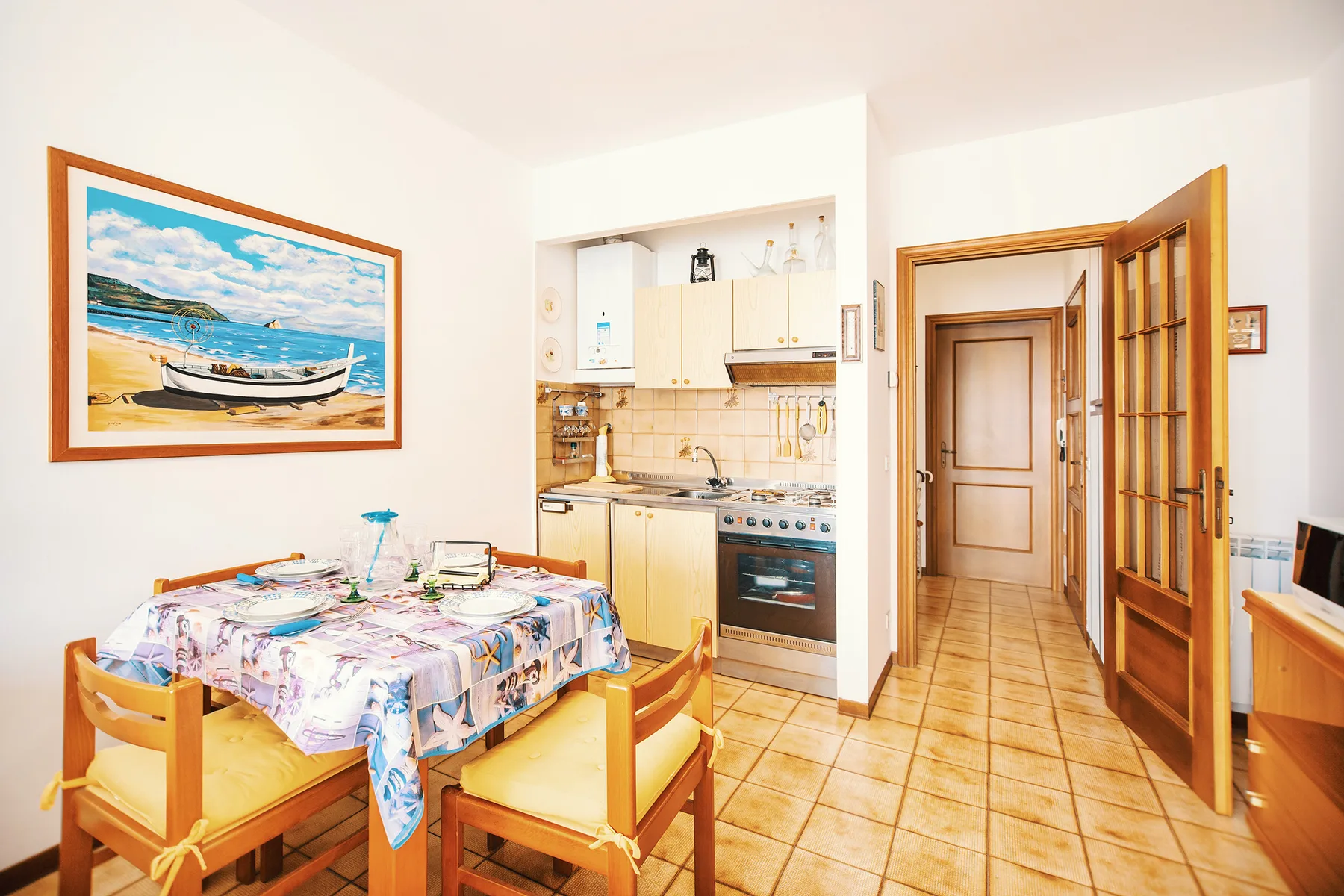 Comedor con una mesa puesta junto a una cocina compacta y un pasillo.