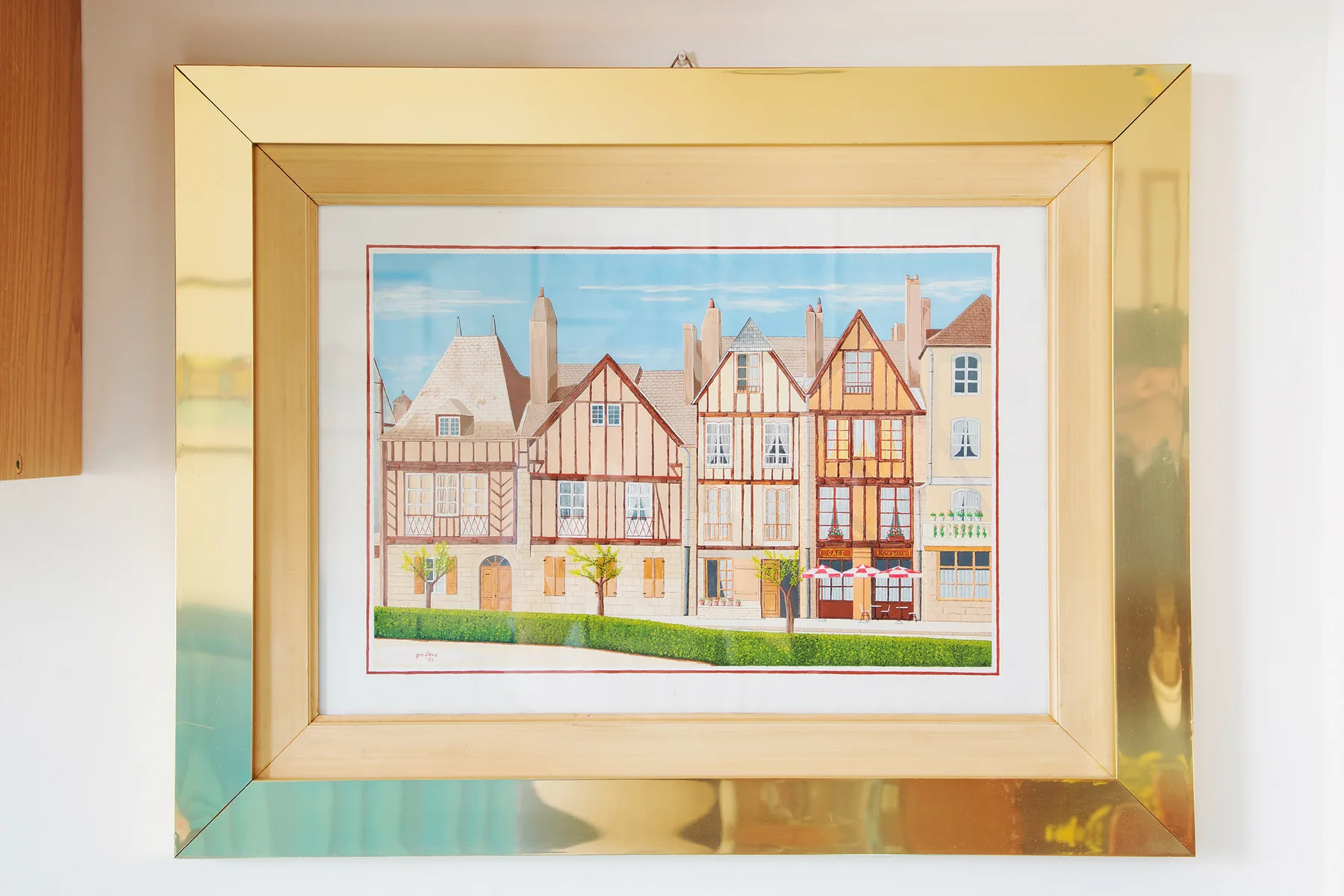 A framed illustration of colorful historic-style buildings hangs on a white wall.