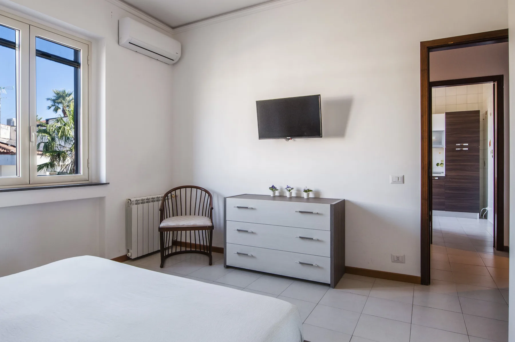 A bright bedroom with a bed, a dresser, and a wall-mounted television.
