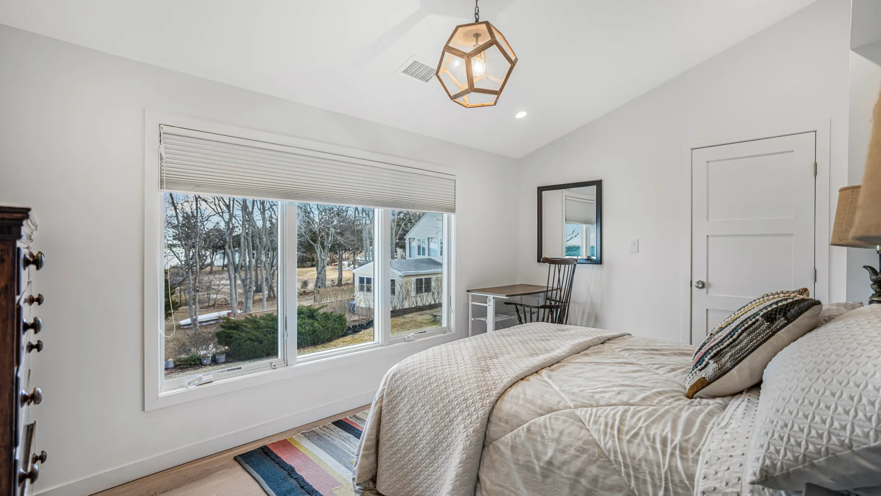 Un dormitorio luminoso con una ventana grande que da a árboles y casas vecinas.