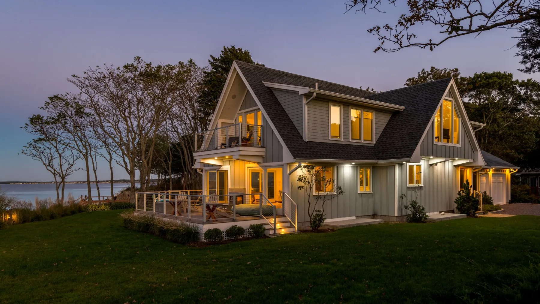 Una casa grande al anochecer resplandece con luz cálida junto a un césped.