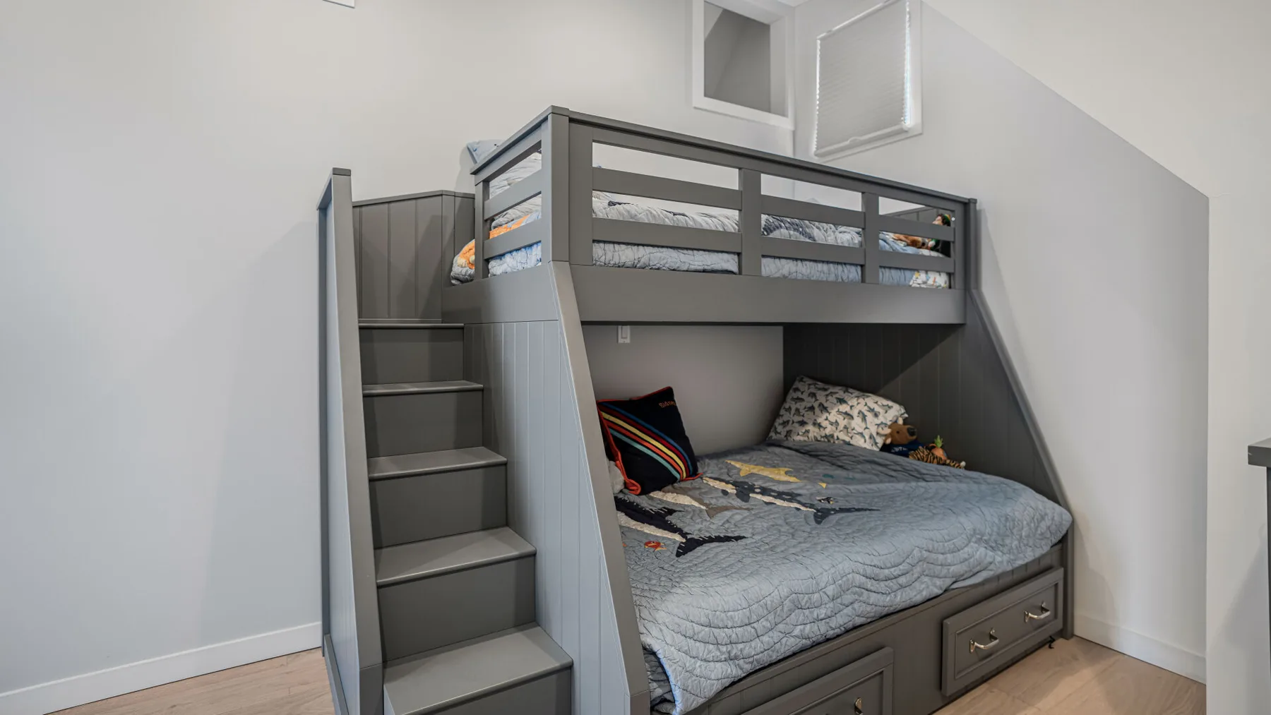 Una litera gris con escalera y ropa de cama ocupa este dormitorio luminoso.