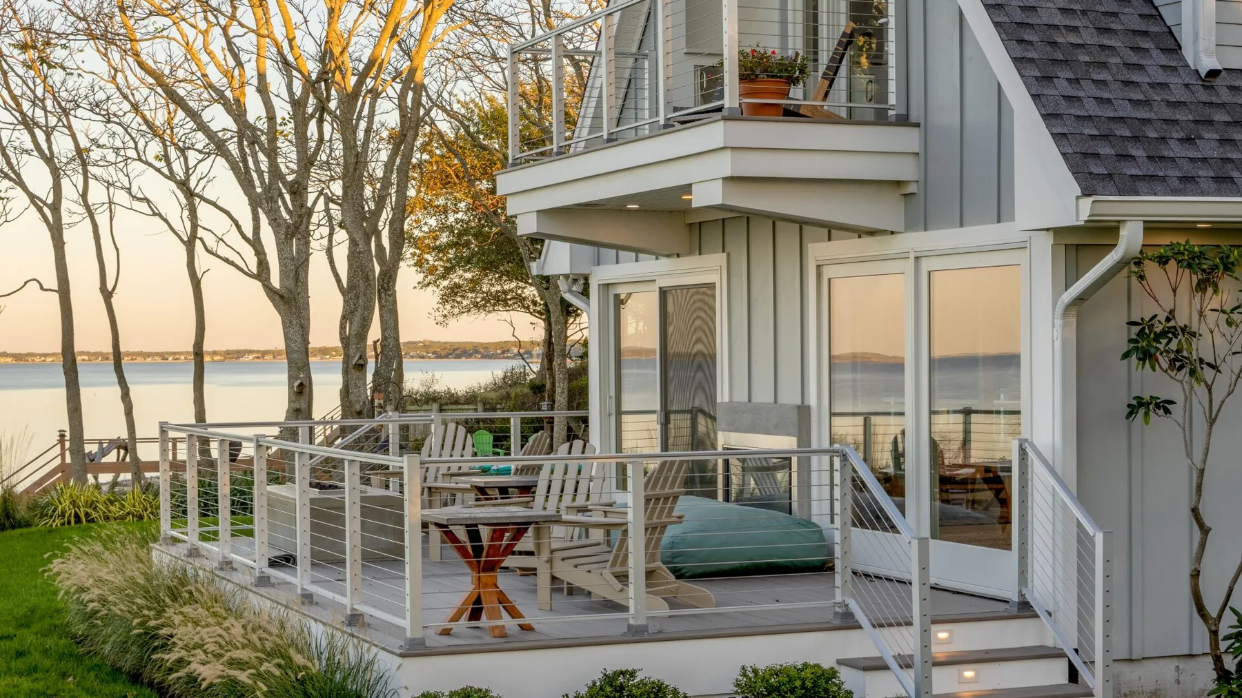 Una casa junto al agua con una terraza elevada, asientos al aire libre y agua tranquila al fondo.