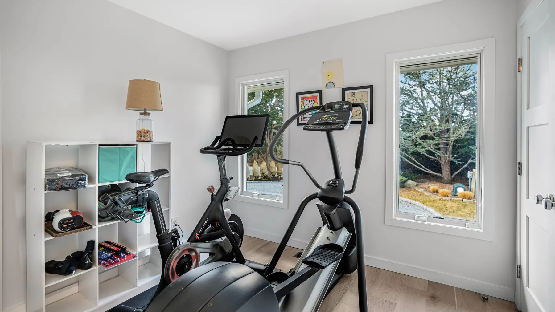 Una sala de ejercicio en casa con equipos de cardio junto a las ventanas.
