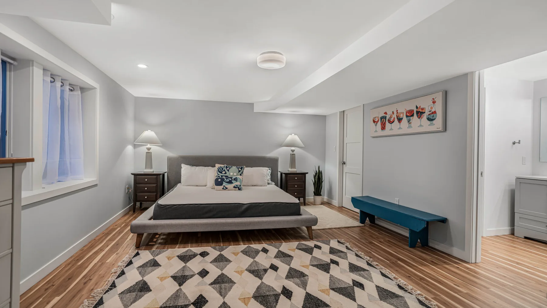 Un dormitorio con una cama, una alfombra estampada y un banco azul.