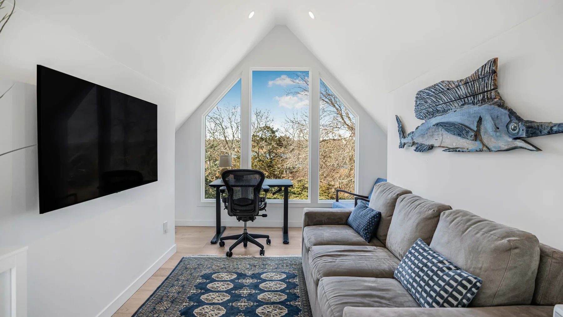 Una sala luminosa con una ventana grande, asientos y un televisor montado en la pared.