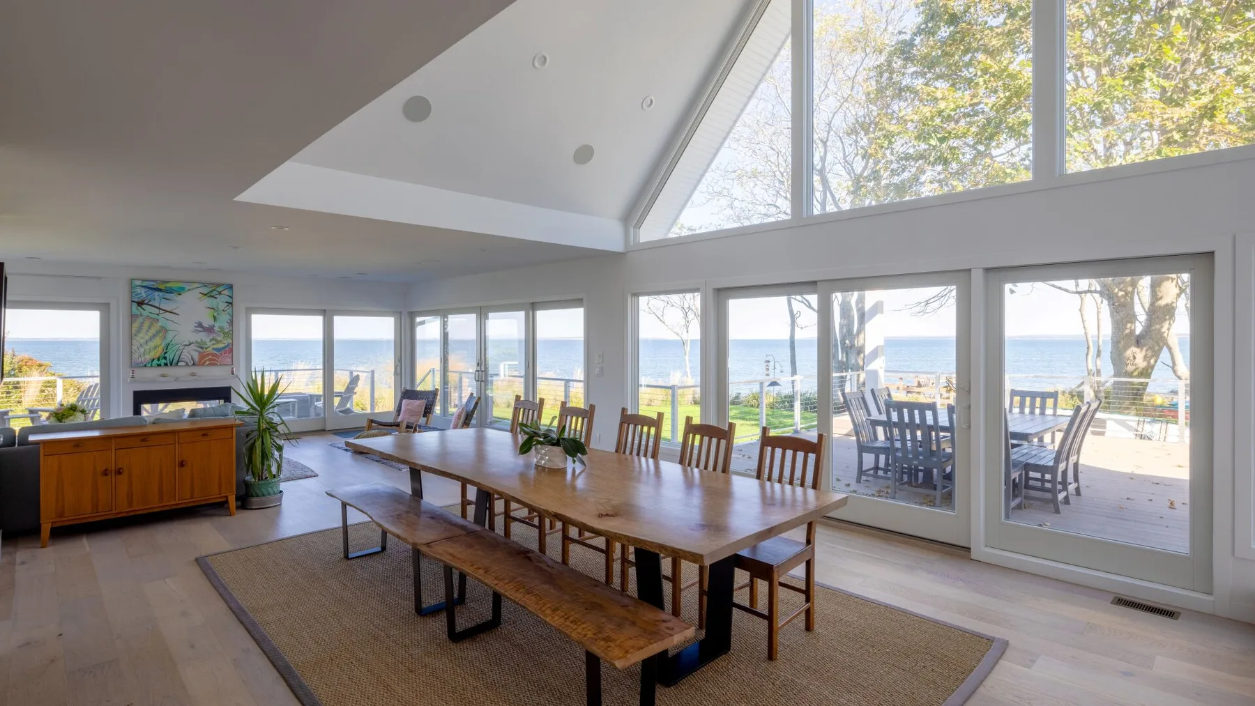 Un comedor luminoso con una mesa larga de madera junto a grandes ventanales con vistas al agua.