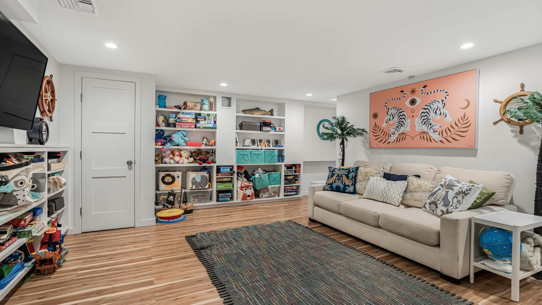Una sala luminosa con sofá beige, alfombra estampada y estantes coloridos.