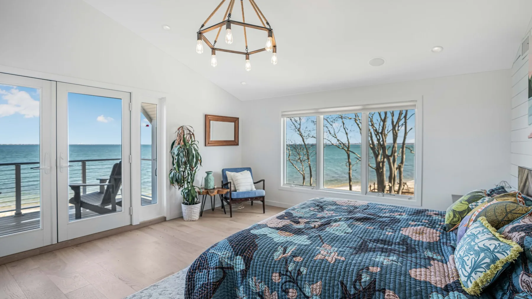 Un dormitorio luminoso con una cama junto a grandes ventanas con vistas al agua.