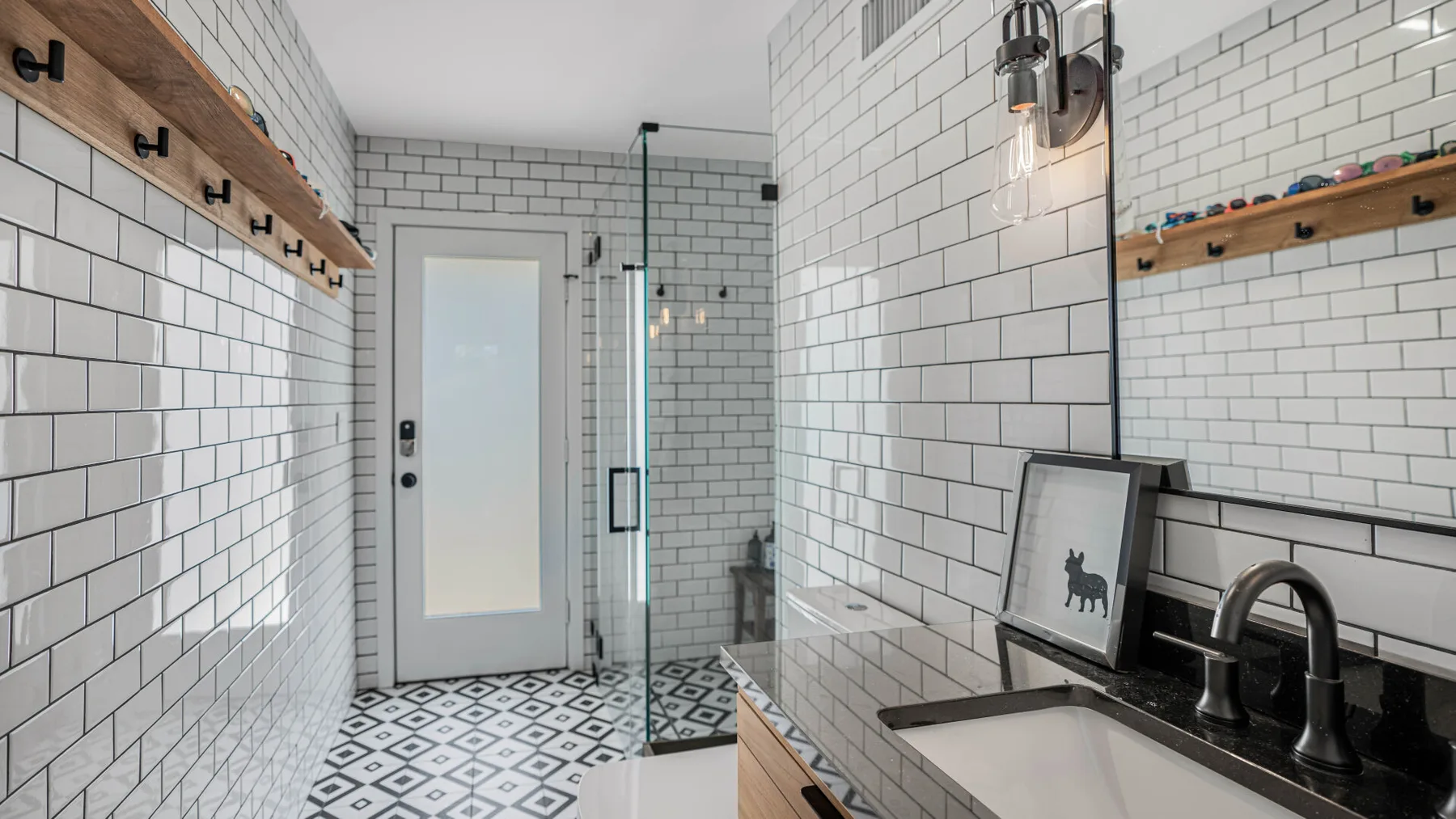 Un baño revestido de azulejos con ducha de vidrio, lavabo y suelo geométrico.