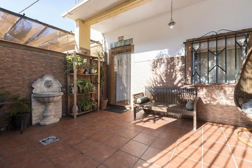 A sunlit tiled courtyard with a wooden bench and potted plants.