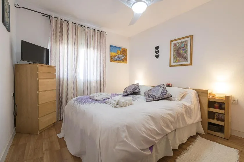 A bright bedroom with a large bed, patterned curtains, and wooden furnishings.