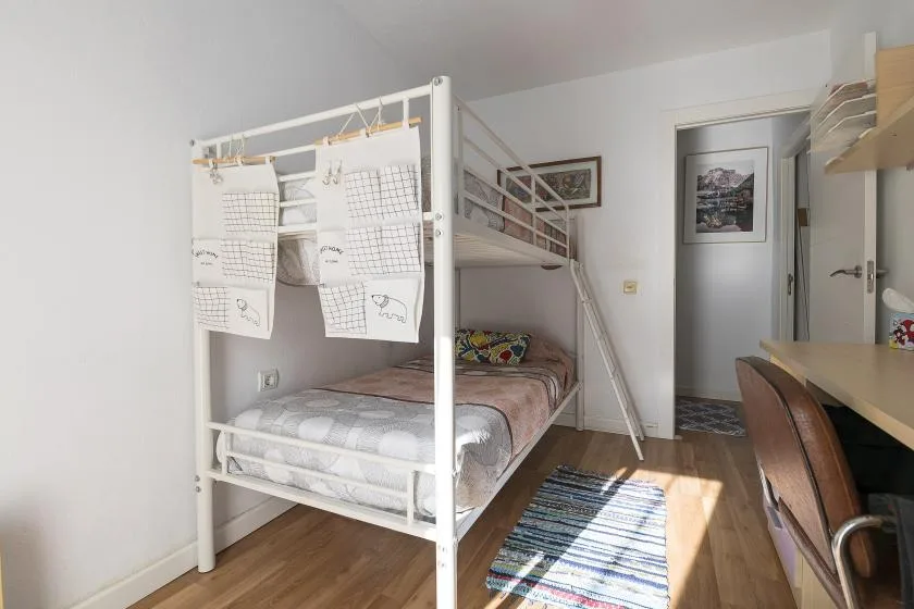 A bright bedroom with a white bunk bed, a desk, and a striped rug.