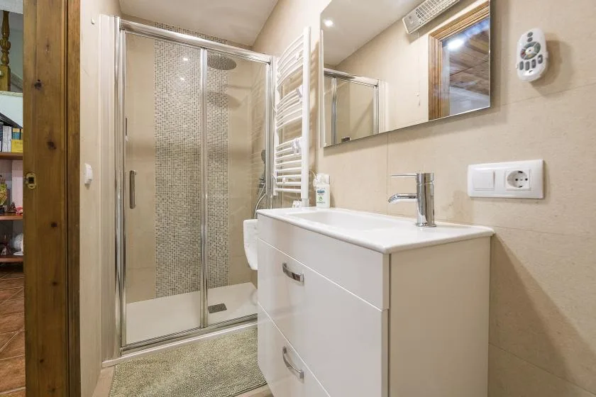 A bathroom with a sink vanity, wall mirror, and glass shower.