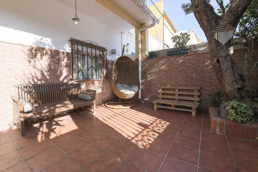 A tiled outdoor patio with a hanging seat, benches, and a large tree.