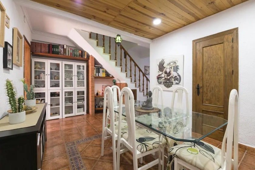 A dining area with a glass table and white seating beside a staircase.