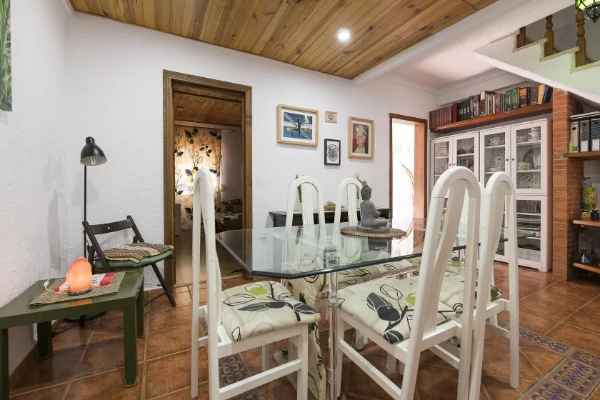 A dining area with a glass table and white seating beneath a wood-paneled ceiling.