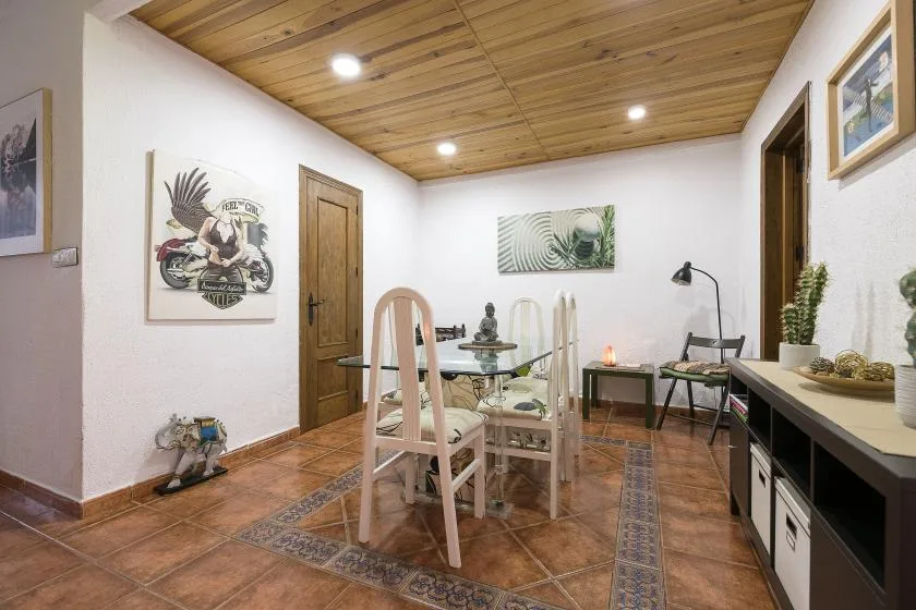 A dining area with a glass table, chairs, and wooden ceiling.