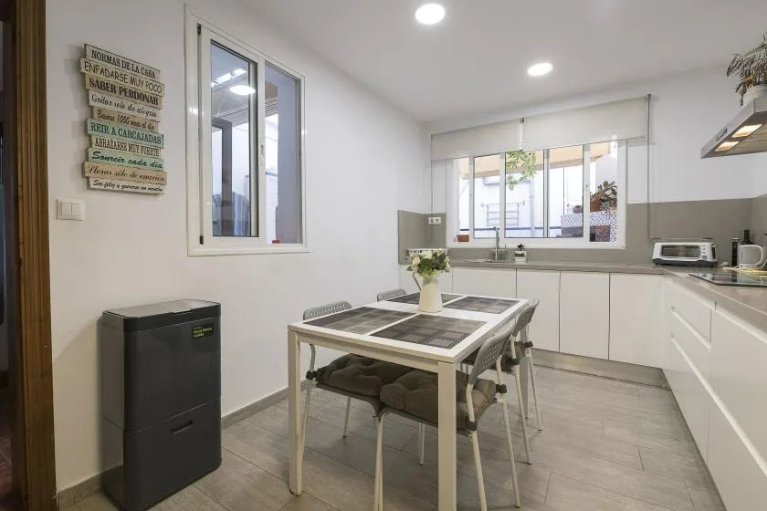 A bright kitchen with a dining table and white cabinets beneath the windows.