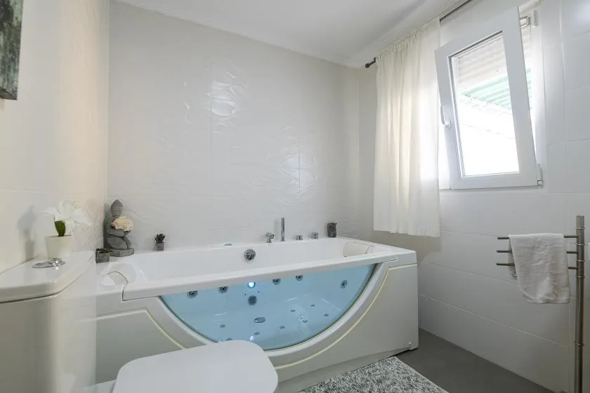 A bright bathroom with a bathtub beneath a window and sheer curtains.