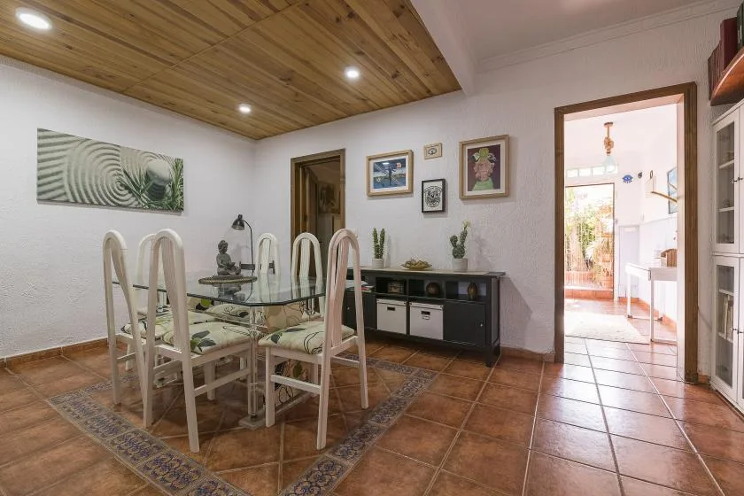 A dining area with a glass table and chairs beneath a wood-paneled ceiling.