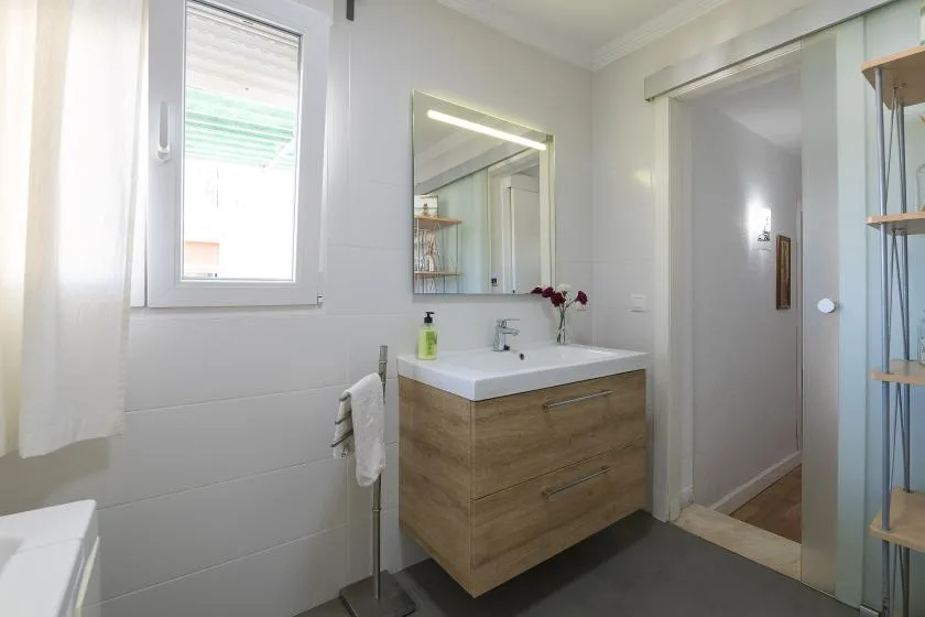 A bright bathroom with a wood-toned vanity and a mirror above the sink.