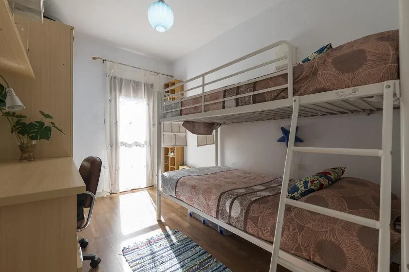 A bedroom with bunk beds, a desk, and a bright window.