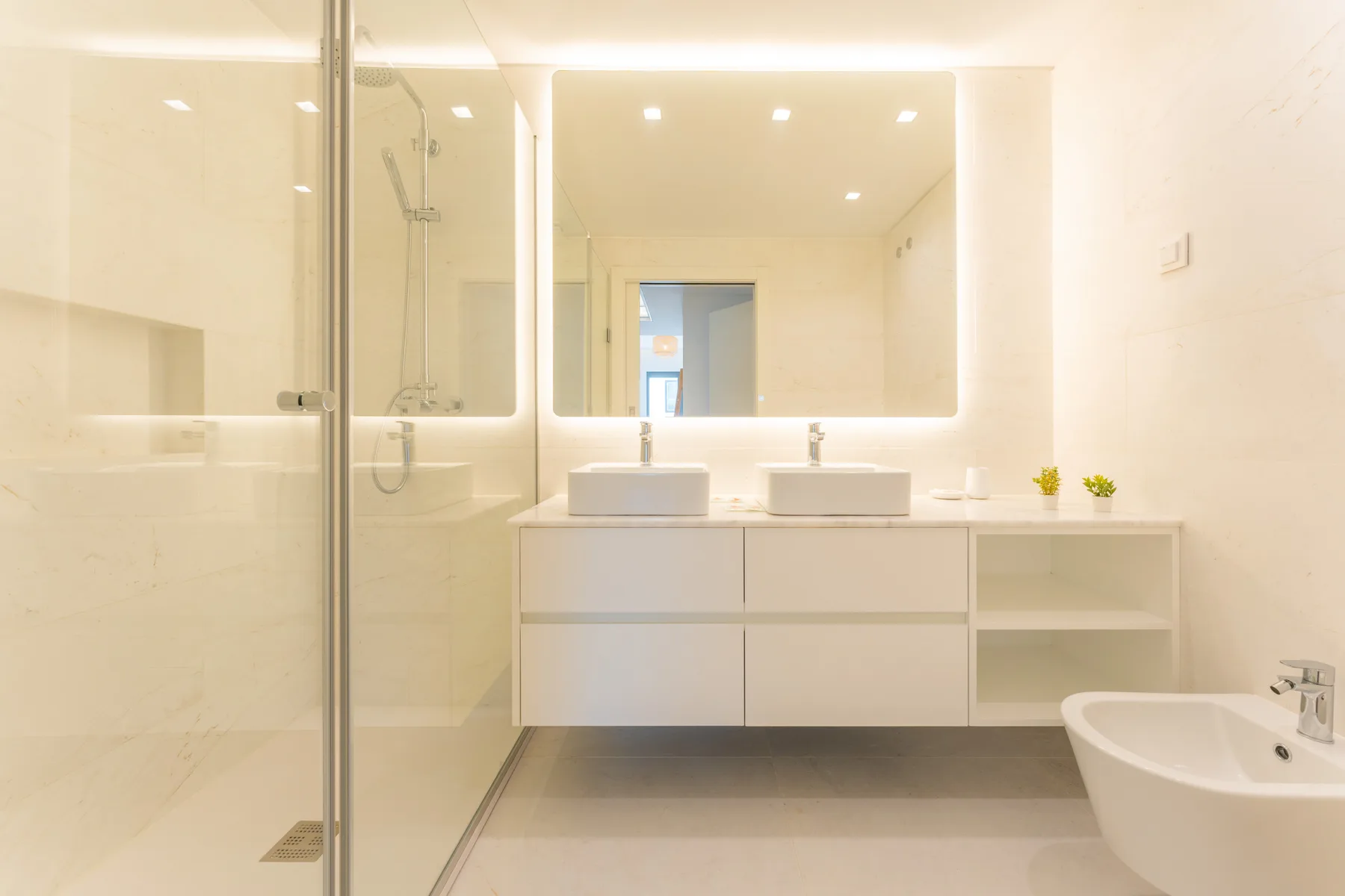 Baño luminoso con ducha de cristal y mueble con dos lavabos.